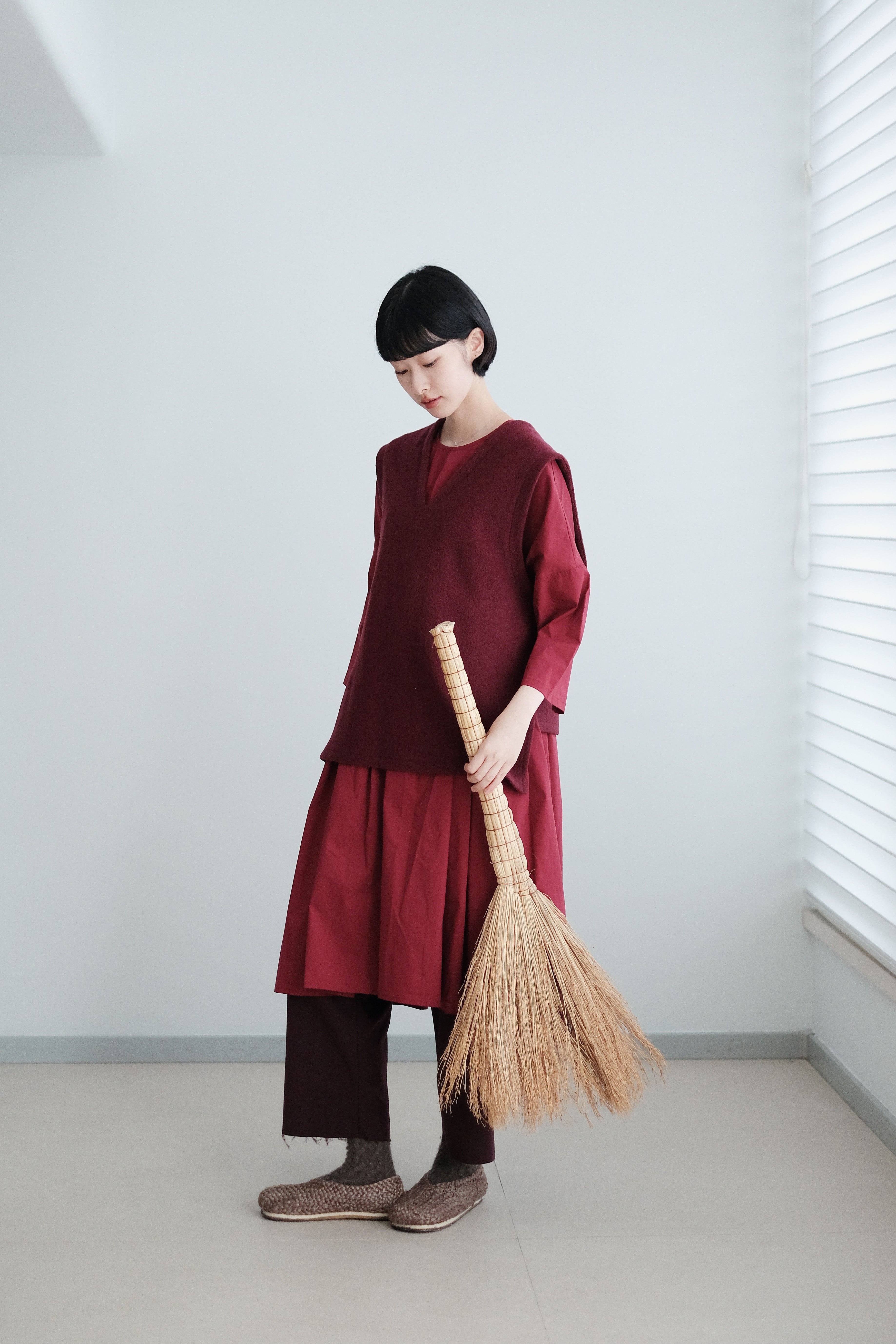 Person wearing a red outfit holding a broom in a minimalistic room.